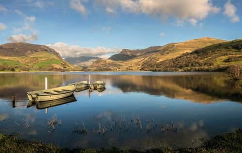 Fishing boats on Llyn Nantlte on a calm evening with a layer of cloud over Snowdon in the distance, Nanttle, North Wales, UK, April