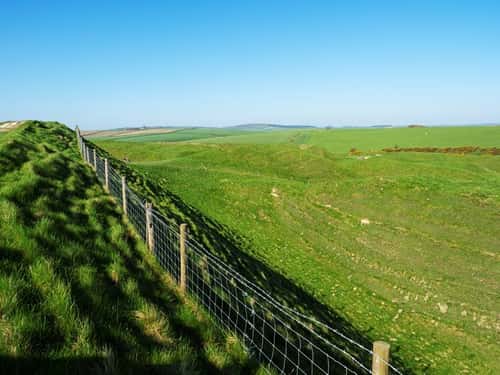 Ramparts of Maiden Castle Iron Age Hill Fort with farmland beyond, near Dorchester, Dorset, England, UK, April
