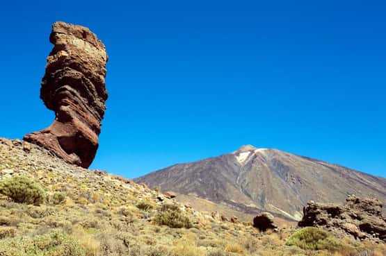 Pico del Teide, iconic rock pinnacle on region known as Roques de Garcia is formed from volcanic intusive dyke below main volcano, the largest mountain in Spain (3,718m) with sub-tropical shrubs growing in caldera floor with semi-arid landscape with rugged aa lava flows, Tenerife, Canary Islands, April