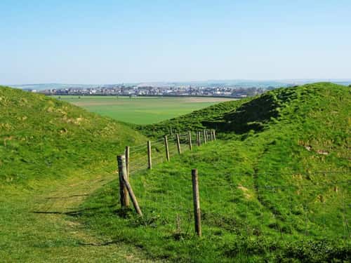 Looking across the ramparts of Maiden Castle Iron Age Hill Fort to the town of Poundbury beyond, Dorset, England, UK, April